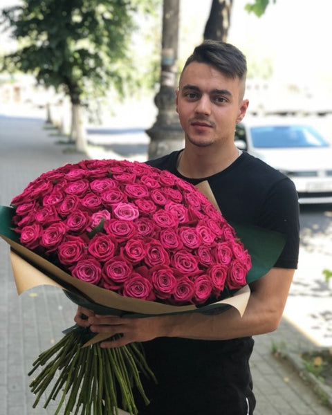 Man holding a large bouquet of vivid pink roses outdoors
