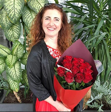 Smiling woman holding a bouquet of red roses near greenery