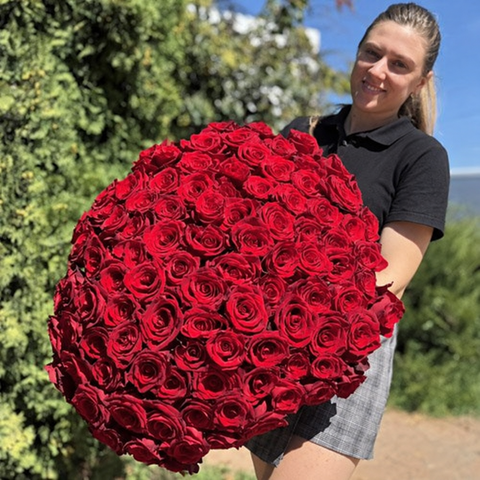 Woman smiling with a bouquet of red roses outdoors