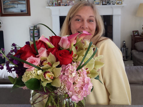 Woman smiling behind a vase of roses, orchids and hydrangeas