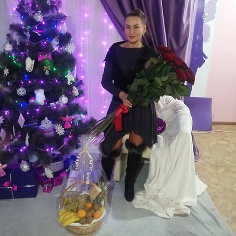 Woman with long red roses and a basket of fruit beside a Christmas tree