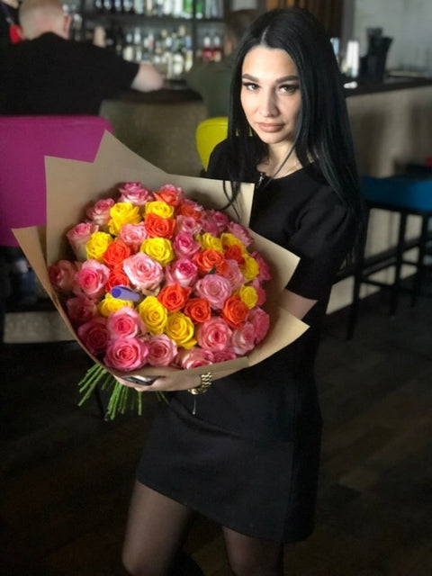 Woman holding a bouquet of yellow, orange and pink roses