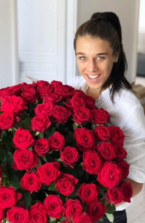 Woman smiling behind a large bouquet of red roses